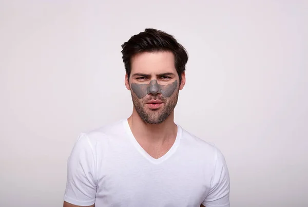 Homem barbudo jovem grave com uma máscara cosmética para o rosto em um fundo leve . — Fotografia de Stock