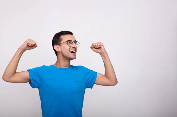 Um jovem de óculos e uma camiseta azul celebra a vitória . — Fotografia de Stock
