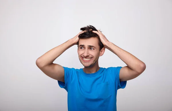 Um cara animado com uma camiseta azul está segurando a cabeça . — Fotografia de Stock