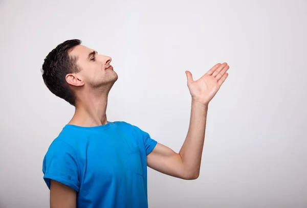 O jovem bonitinho alegre em uma camiseta azul mostra sua direção da mão . — Fotografia de Stock