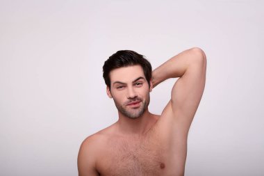 Yakışıklı esmer kurnazca gülümsüyor ve elini başının arkasında tutuyor.