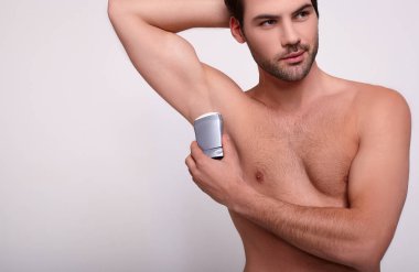 Yakın plan, bir adam sağ koltuk altına deodorant sürüyor..