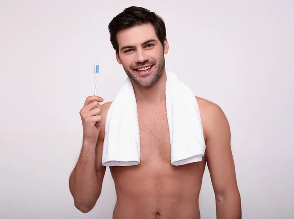 A smiling man after a shower with a toothbrush in his hands.