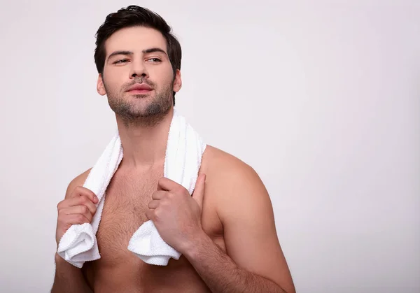 Νεαρός σέξι άντρας ποζάρει με λευκή πετσέτα σε γκρι φόντο. — Φωτογραφία Αρχείου