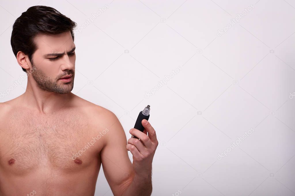 A brooding young guy shirtless with a trimmer in his hand.