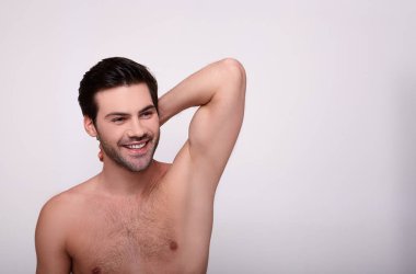 Havalı siyah saçlı adam gülümsüyor ve yana bakıyor.