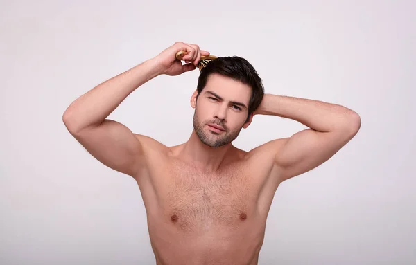 A muscular shirtless guy combs his hair with a comb.