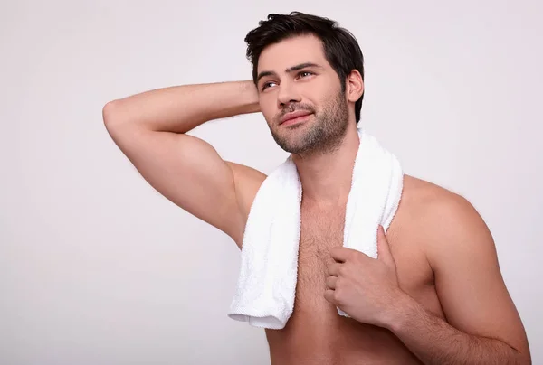 Un joven sin camisa con una toalla blanca alrededor de su cuello mira a un lado . — Foto de Stock