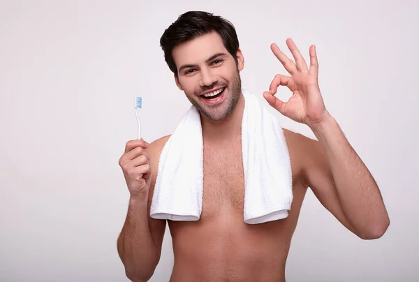 Hezký muž s bílým ručníkem si čistí zuby a dává najevo, že je v pořádku. — Stock fotografie