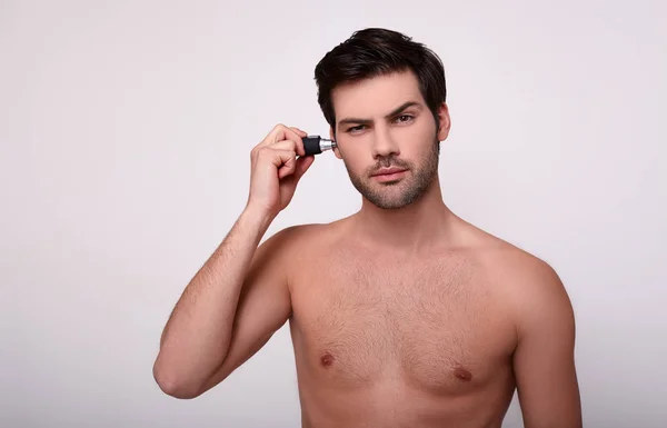 Okouzlující muž bez trička odstraňuje nechtěné vlasy s trimrem. — Stock fotografie