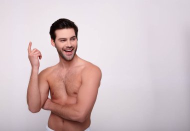 Havluyla kaplanmış, gülümseyen, gri arka planda duran sevimli, üstsüz genç adam..