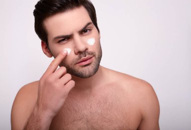 Yakın plan, genç bir adam yüzüne krem sürüyor..