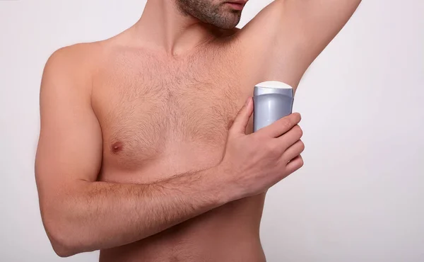 Handsome young man applying deodorant in room.