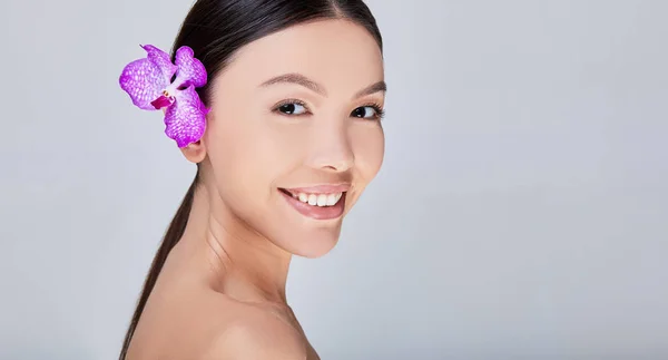 Mosolygó ázsiai nő lila orchideával a füle mögött — Stock Fotó