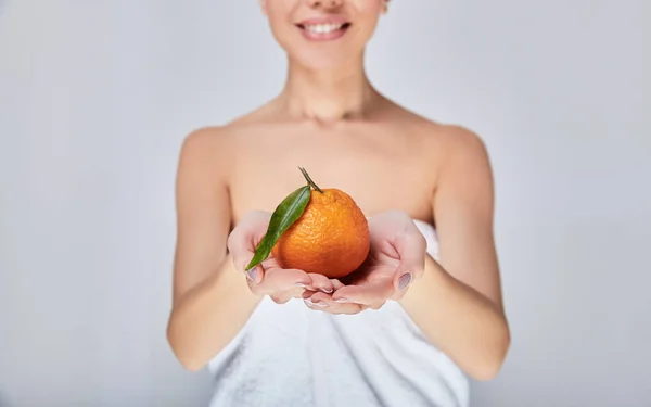 The woman in the white towel holds an orange in her hand. — ストック写真