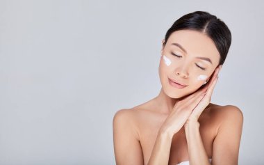 Delicate romantic Asian woman with cream on her face closed her eyes.