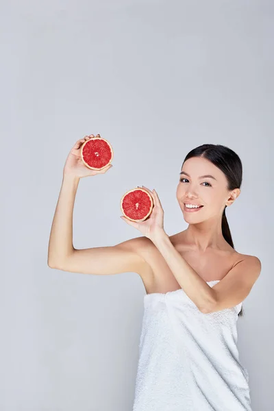 Sexy asian woman posing in studio with halves of grapefruit. — Stock Photo, Image