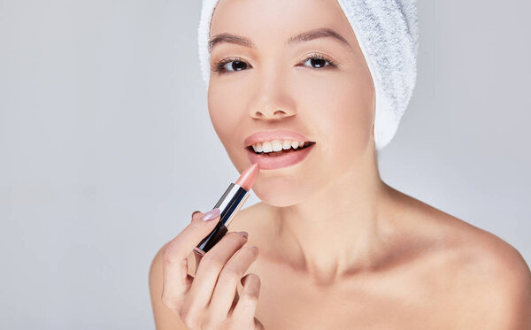 A close-up of a young Asian woman paints her lips with lipstick.