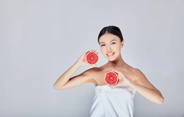 A young beautiful Asian woman after a shower holds in the hands of greffruit, citrus, Sicilian orange. — Stock Photo, Image