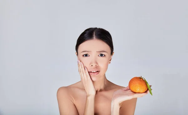 A surprised Asian woman holds an orange in her hand. — Stock Photo, Image