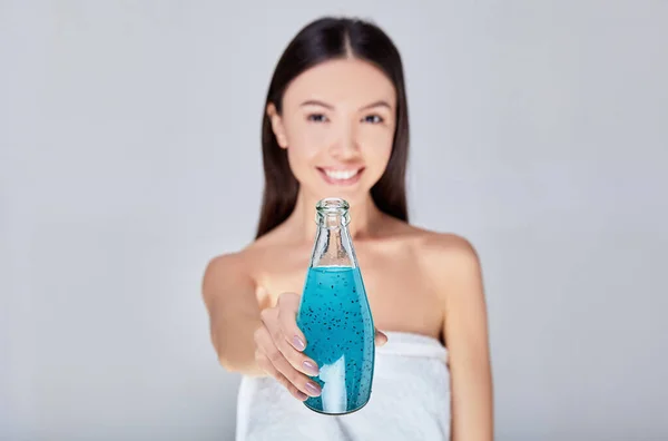 A cute Asian woman after a shower drinks a fruit cocktail of blue color. — Stock Photo, Image