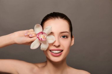 Joyful young brown-haired woman with a flower of white orchid near the face.