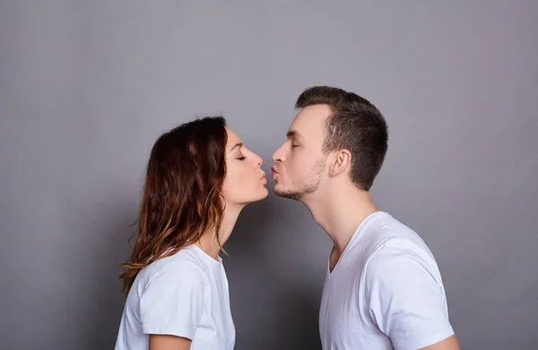 Una joven pareja caucásica cariñosa beso sobre un fondo gris . — Foto de Stock