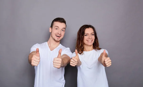 Hermosa pareja joven sobre un fondo gris muestra el dedo como signo . — Foto de Stock