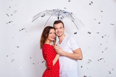 Neşeli, neşeli, güzel, beyaz bir çift, birlikte mutlular, gülüyorlar, şemsiye altında saklanıyorlar konfeti düşmekten, öpüşmekten, beyaz bir arka planda izole edilmiş..