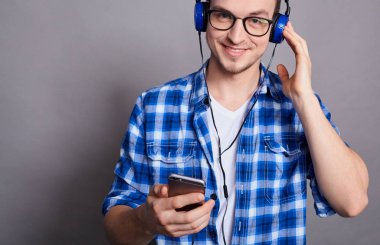 Kırpılmış çerçeve, gözlüklü, beyaz tişörtlü, kafeste mavi tişörtlü, elinde telefon tutan ve mavi kulaklıkla müzik dinleyen beyaz bir genç..