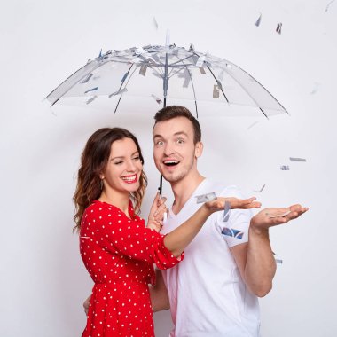 Şatafatlı, zarif, birbirine aşık genç bir çift, gülüyorlar, şemsiye altında saklanan bir çift konfetiye sarılıyorlar, konfeti yakalıyorlar, ellerini beyaz arka planda yalnız bırakıyorlar..