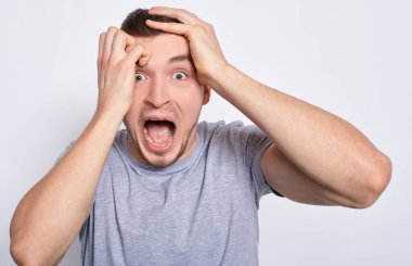 Yakından, gri tişörtlü genç çekici bir adam beyaz arka planda poz veriyor, takımı kazanırken ya da kaybederken çığlık atıyor. Bir adamın fotoğrafı, haberden şok olmuş, çığlık atıyor, başını elinde tutuyor..