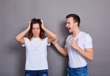 Bıyıklı, beyaz tişörtlü ve kot pantolonlu bir çift genç kadın ve adam. Düşman mavi arka planda izole bir şekilde duruyor. İlişki krizi kavramı.