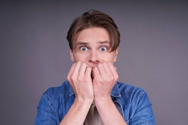 Yakışıklı, hippi, kot tişörtlü ve bej tişörtlü, korkmuş görünüyor, ellerini ağzının yanında tutuyor. İnsanların yaşam tarzı konsepti. Düzen kopyalama alanı.