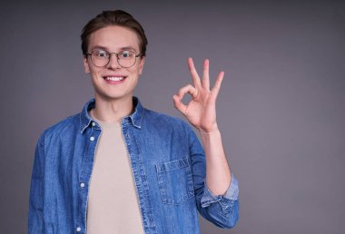 Mavi kot ceketli, neşeli, neşeli, gülümseyen, el kol hareketi yapan, iyi bir işaret gösteren genç, yakışıklı adam. Kafkasyalı adam parmaklarıyla hareket ediyor, sağ arka planıyla işaret veriyor..