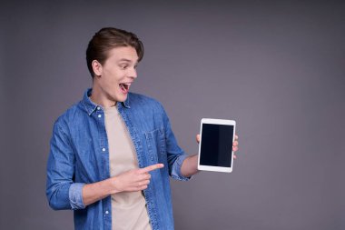 Kot pantolonlu neşeli, pozitif, çekici bir adamın portresi, elinde akıllı bir telefon, elinde siyah bir ekranla tablet, ürünü işaret ediyor ve heyecanla bağırıyor..