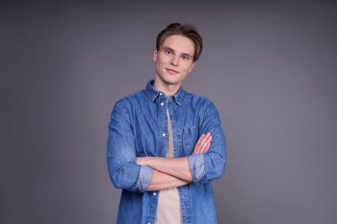 Hırslı bir adam kollarını kavuşturmuş, sanki gri bir arka planda izole edilmiş bir iş geliştirme stratejisi planlıyormuş gibi yoldan çekiliyor. Boşluğu kopyala.