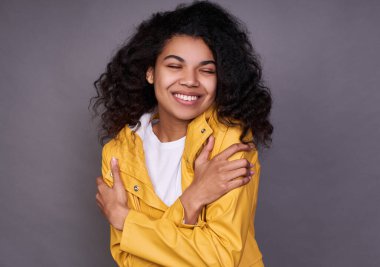 Hassas, genç, siyah kıvırcık saçlı, beyaz tişörtlü, sarı ceketli genç ve narin bir kız. Kollarıyla kendine sarılıyor. Rüyasında gözlerini kapayıp gülümsüyor..