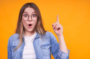 Beyaz tişört ve kot ceketli beyaz bir fikir bulan sevimli, çekici, beyaz bir kız, işaret parmağıyla, Hope 'la üstünü gösteriyor..