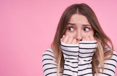 Heyecanlı genç bir manken elleriyle ağzını kapatıyor. Yeni olaylardan korkan bir şey. Pembe arka planda çizgili bir kazak. İnsani duygular korkusu kavramı. Uzayı kopyala..