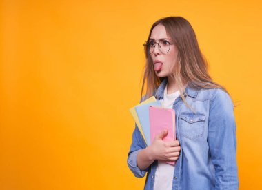 Çok renkli elleri, gözlüğü ve sarı arka planda kot ceketi olan komik, sevimli bir öğrenci, boş fotokopi alanı ile sol tarafa döndü..