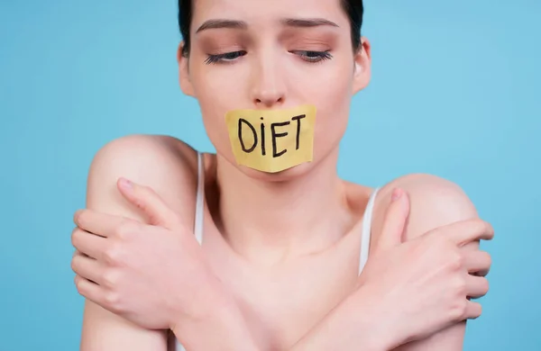 Young woman with taped mouth with the word diet. Diet concept. Weight loss problem. Hungry young woman. Sealed mouth. Tape with the word. Hungry woman. Healthy lifestyle concept.