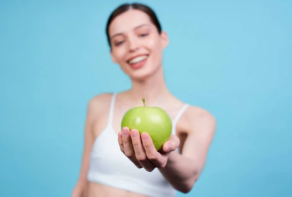 かわいい魅力的な笑顔の若い白人の女の子は 白い上に 青い背景にポーズをとって 彼女の外側の腕の上にジューシーな緑のリンゴを保持しています 健康的な食事 果物の概念 — ストック写真