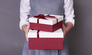 Gri bir arka planda beyaz bir süveter içinde uzun zamandır beklenen sürprizi veren ya da alan bir çocuğun nazikçe ve nazikçe tuttuğu kırmızı-beyaz hediye kutusunun portresi. Boşluğu kopyala.