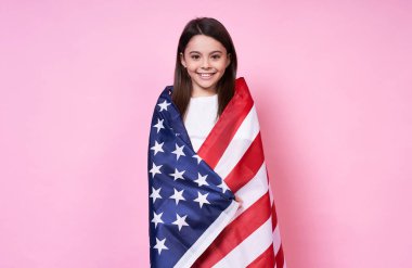 Komik stil sahibi, genç duygusal kız, uzun saçlı esmer, gülümseyen, kendini Amerikan bayrağı ile kaplamış, Bağımsızlık Günü, 4 Temmuz, zafer, ABD, pembe arka planda beyaz bir tişört..