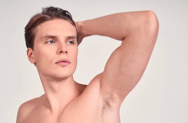 Yakışıklı, çekici bir genç, çıplak, sarı saçlı, mavi gözlü, sağlıklı tenli, kollarında, dirseğinde öne bakan, beyaz bir arka planda duran kasları var..