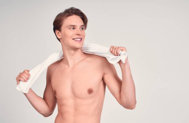 Beyaz bir arka planda, havluyla poz veren ve gülen neşeli, yarı çıplak, beyaz bir beyaz adamın görüntüsü, bir kenara bakıyor. Boşluğu kopyala.