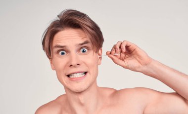 Komik, genç, çıplak beyaz bir adam, modern bir saç stili takıyor, kulağını temizliyor, vücut bakımını yapıyor. Erkek gigiena konsepti.