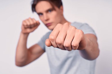 Beyaz arka planda boks yapan, sarı saçlı, gri tişörtlü, beyaz tişörtlü, beyaz saçlı, beyaz tenli genç sporcu, yumruğuna odaklan..