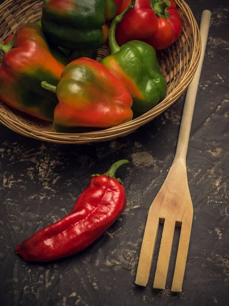 Pipper vermelho e garfo wodden na mesa de pedra na cozinha, com cesta de pimentas verdes — Fotografia de Stock